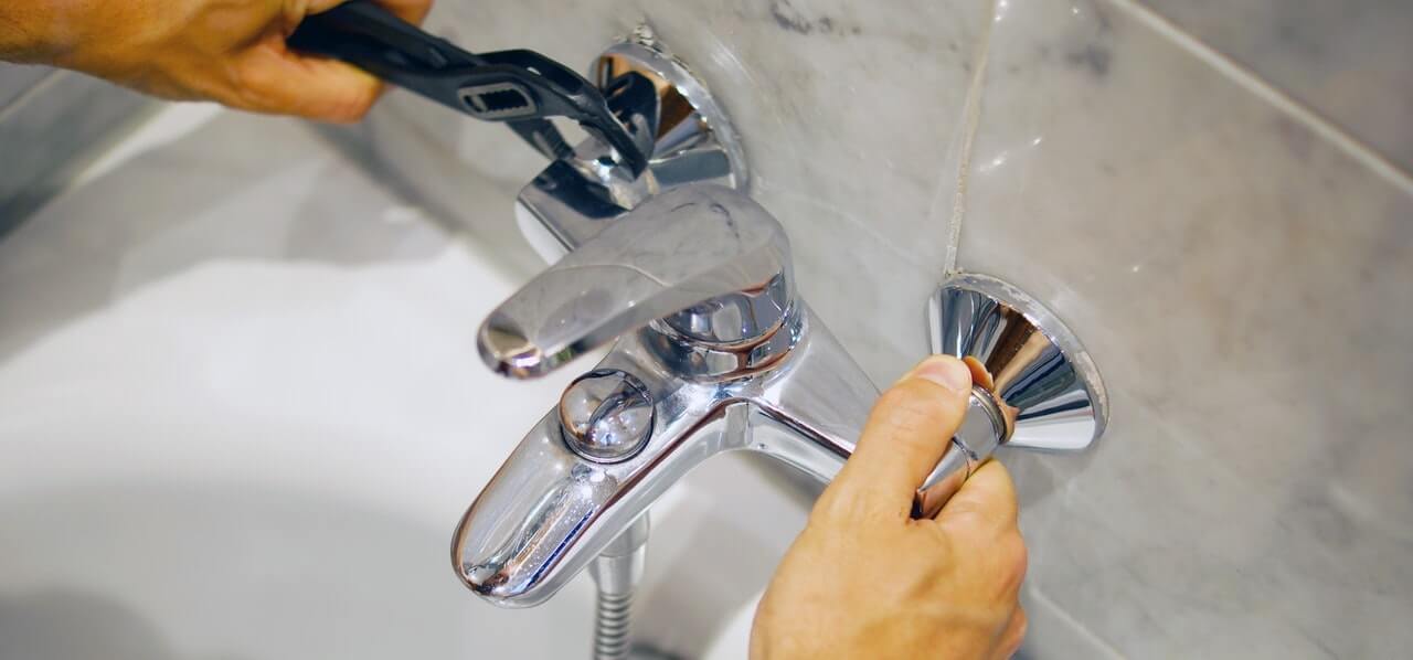 Plumber using a wrench to fit a chrome bath mixer tap during a tap installation