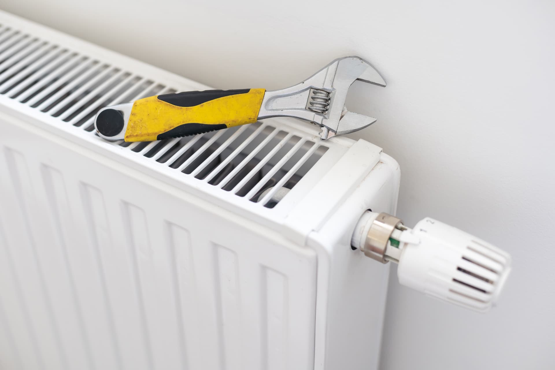Adjustable spanner resting on a white radiator with a thermostatic valve during a central heating repair