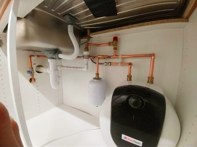 General plumbing work: under-sink water heater with copper pipework, expansion vessel and waste trap beneath a kitchen sink