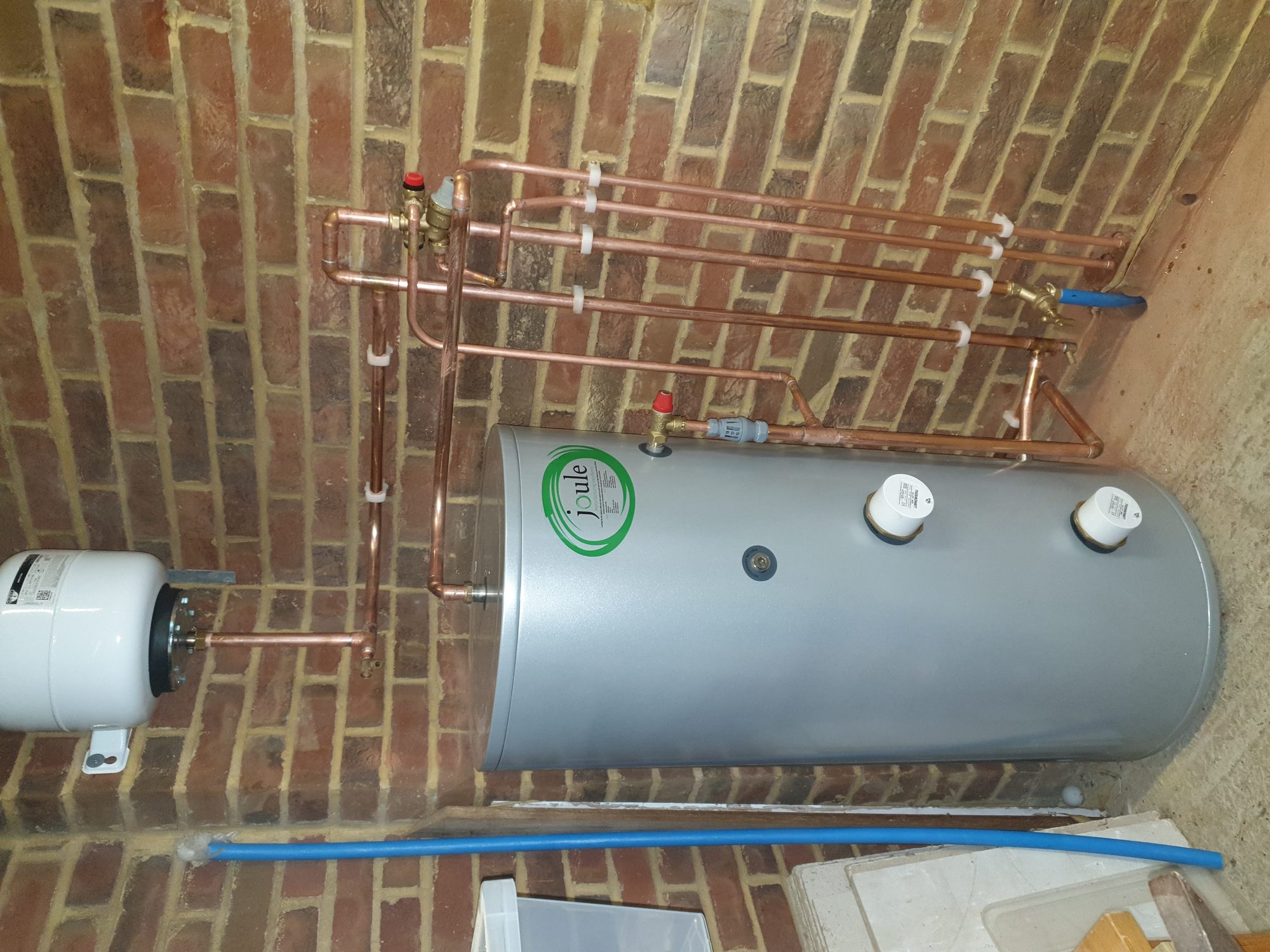 Central heating installation with a hot water cylinder, expansion vessel and clipped copper pipework on brickwork