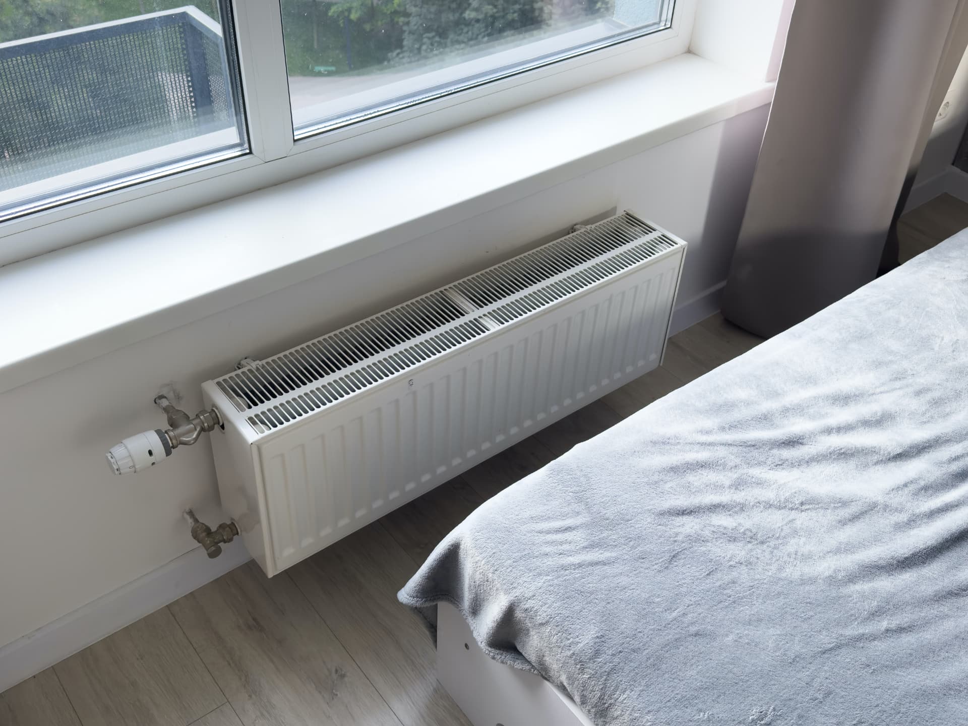 Newly installed white radiator with thermostatic valve under a bedroom window
